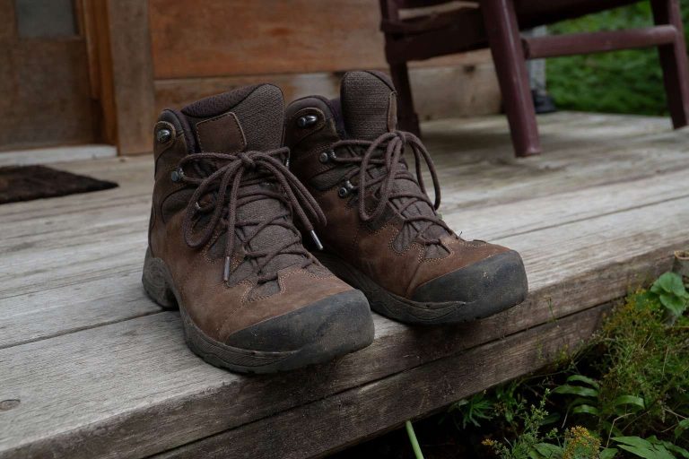A pair of well-used hiking boots resting on a weathered wooden cabin porch step