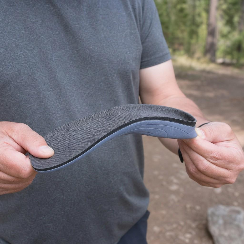 A hand flexing a hiking insole to show its firm arch and heel cup