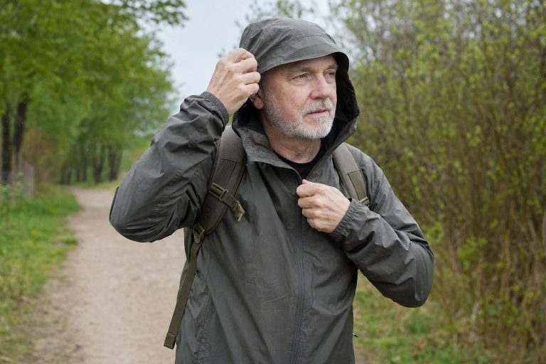 A hiker on an easy trail pulls up the hood of a plain packable rain jacket as light rain begins