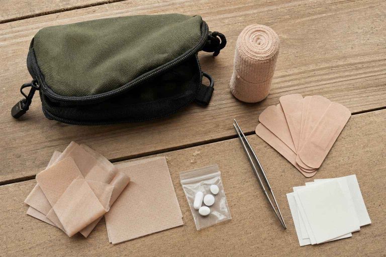 A compact day-hike first-aid kit laid out on a wooden table: bandages, moleskin, elastic wrap and tweezers