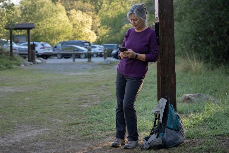 A hiker sends a text at the trailhead before starting out, daypack ready at her feet
