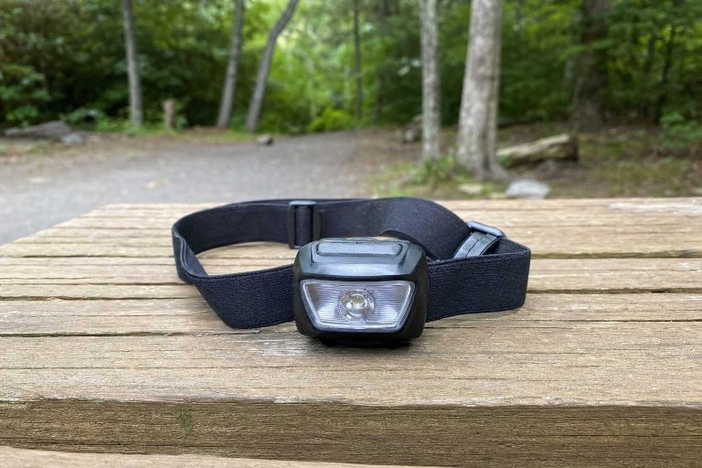 A compact headlamp resting on a wooden trailhead table in soft late-afternoon light