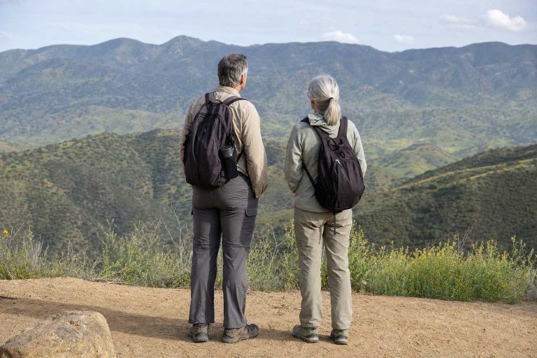 An older couple wearing small daypacks pausing at an easy trail overlook