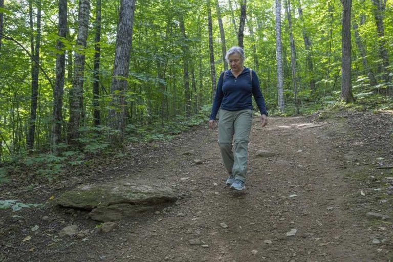 A woman over 50 walking carefully down a gentle forest trail descent