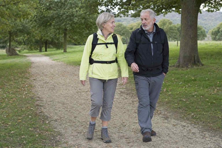 An older couple walking at an easy pace along a flat packed-gravel parkland path