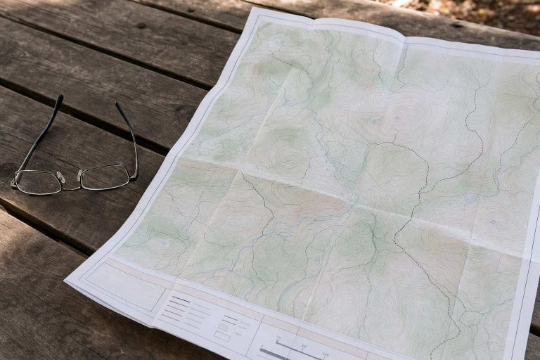 A folded paper trail map and reading glasses on a picnic table at a trailhead