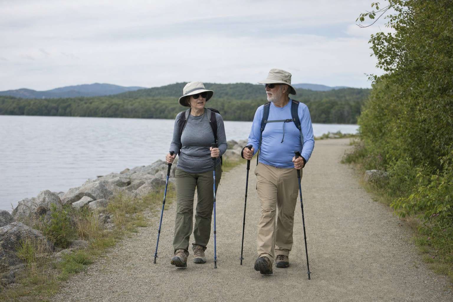 Two older hikers walking toward the camera on a long lakeside trail