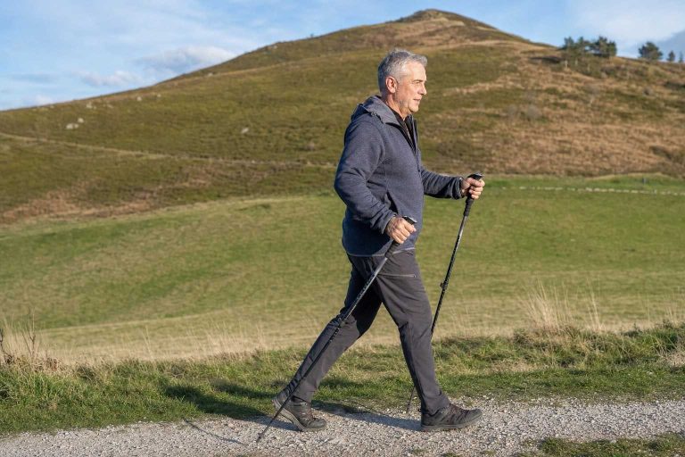 A man over 50 walking with trekking poles in a natural rhythm on an open hillside trail